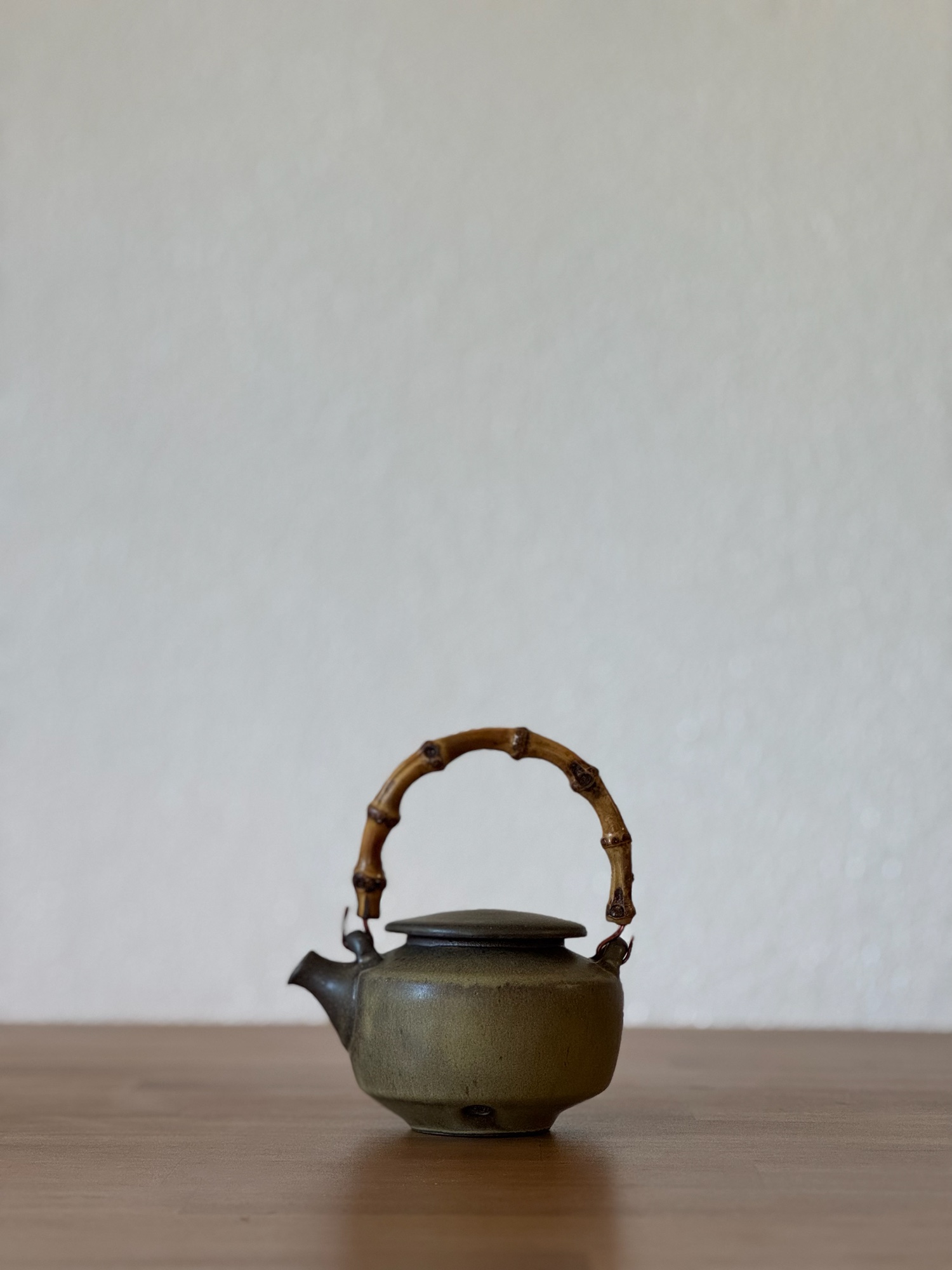 Handmade ceramic teapot with a bamboo handle on a wooden surface