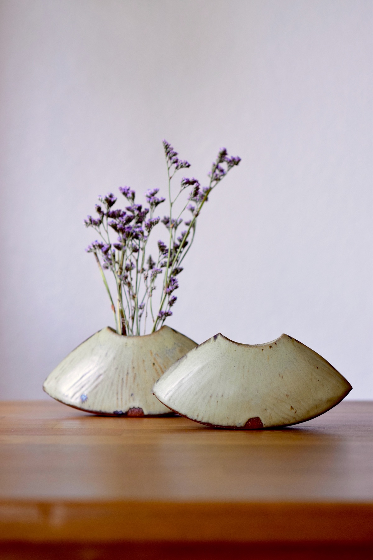 Two low wing-shaped ceramic bud vases, one holding purple flowers