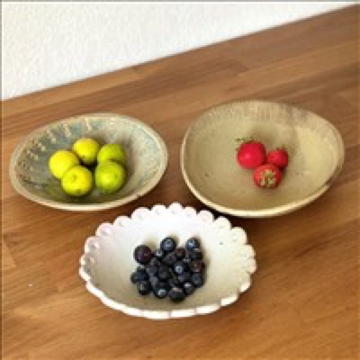 Three handmade ceramic bowls filled with colorful summer fruit