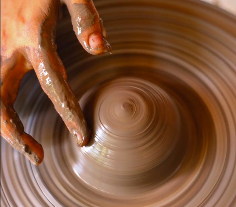 Hands shaping wet clay on a spinning pottery wheel